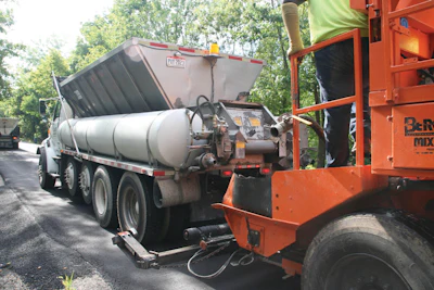A paving crew member connects the Mobile Support Unit’s asphalt emulsion tank and water tank to the slurry paver and opens the gate to the aggregate hopper, allowing the paver to continually place the surface treatment.