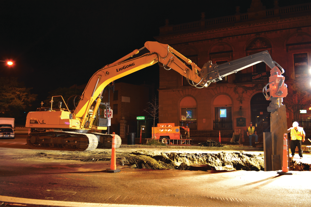 A LiuGong 936D excavator drives an I-beam into the ground to install trench box walls prior to pipeline replacement.