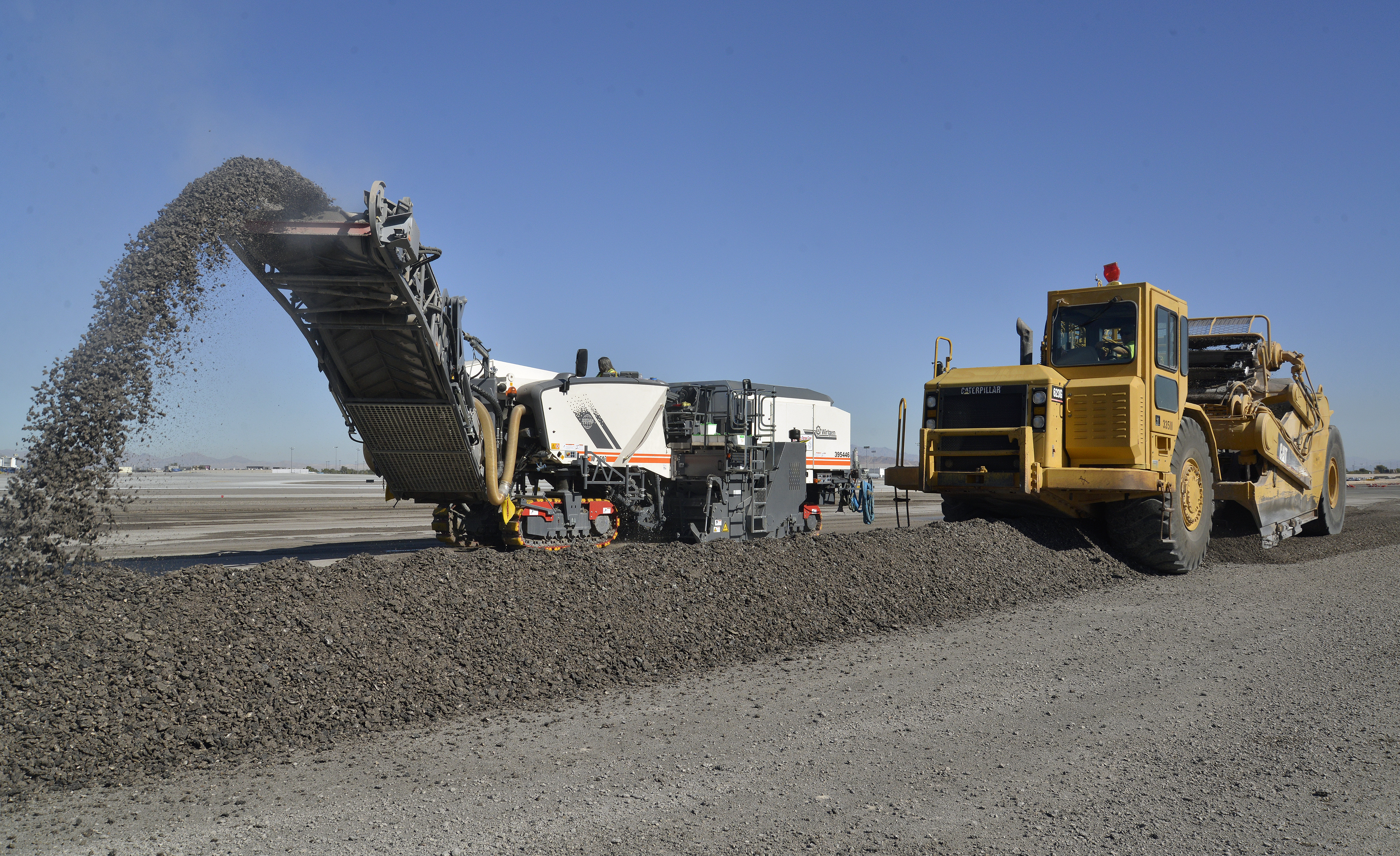 Instead of five to six haul trucks recirculating, Las Vegas Paving uses two paddle wheel scrapers to pick up windrows of RAP and deposit the material on airfield unpaved areas, where it will be compacted and used for erosion control.