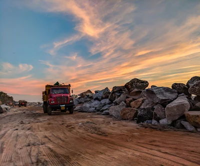 Red Dump Truck Near Filed Rocks Under Cloudy Sky 1044290