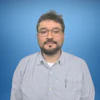 Professional wearing glasses in gray shirt against blue background