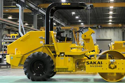 Yellow Sakai industrial road roller in manufacturing facility with overhead crane