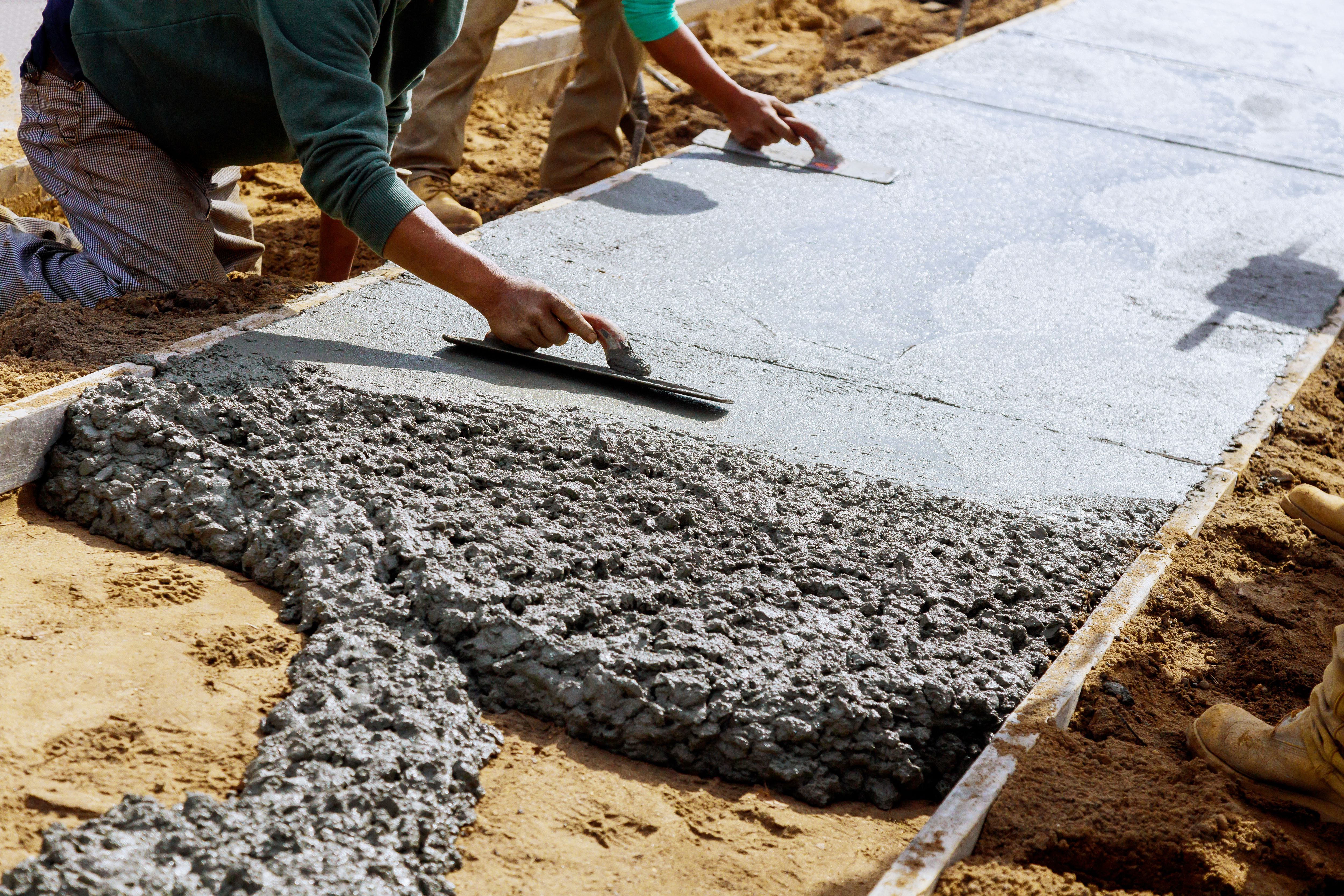 Workers smoothing wet concrete for sidewalk installation using professional trowels
