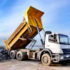 Yellow-topped dump truck unloading rocks at construction site with city skyline