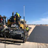 Road construction crew operating asphalt paver on desert highway