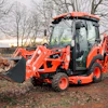 KIOTI CS30 sub-compact tractor with front loader carrying firewood logs in rural setting