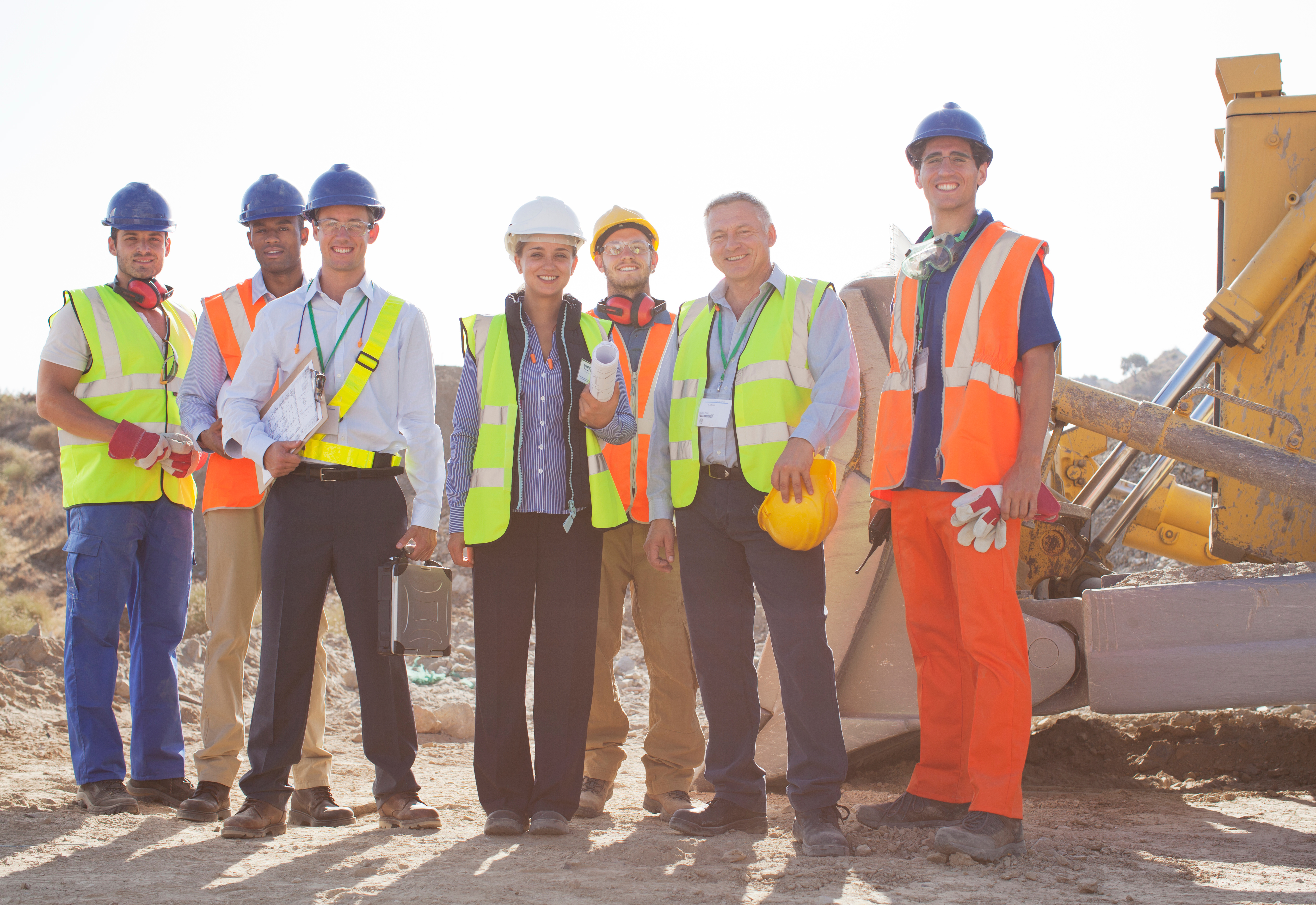 Diverse construction crew in safety gear posing at worksite with heavy equipment
