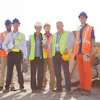 Diverse construction crew in safety gear posing at worksite with heavy equipment