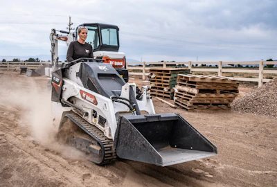 Bobcat tracked loader moving dirt at construction site with dust clouds