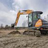 Case excavator digging in muddy field with bare trees and overcast sky