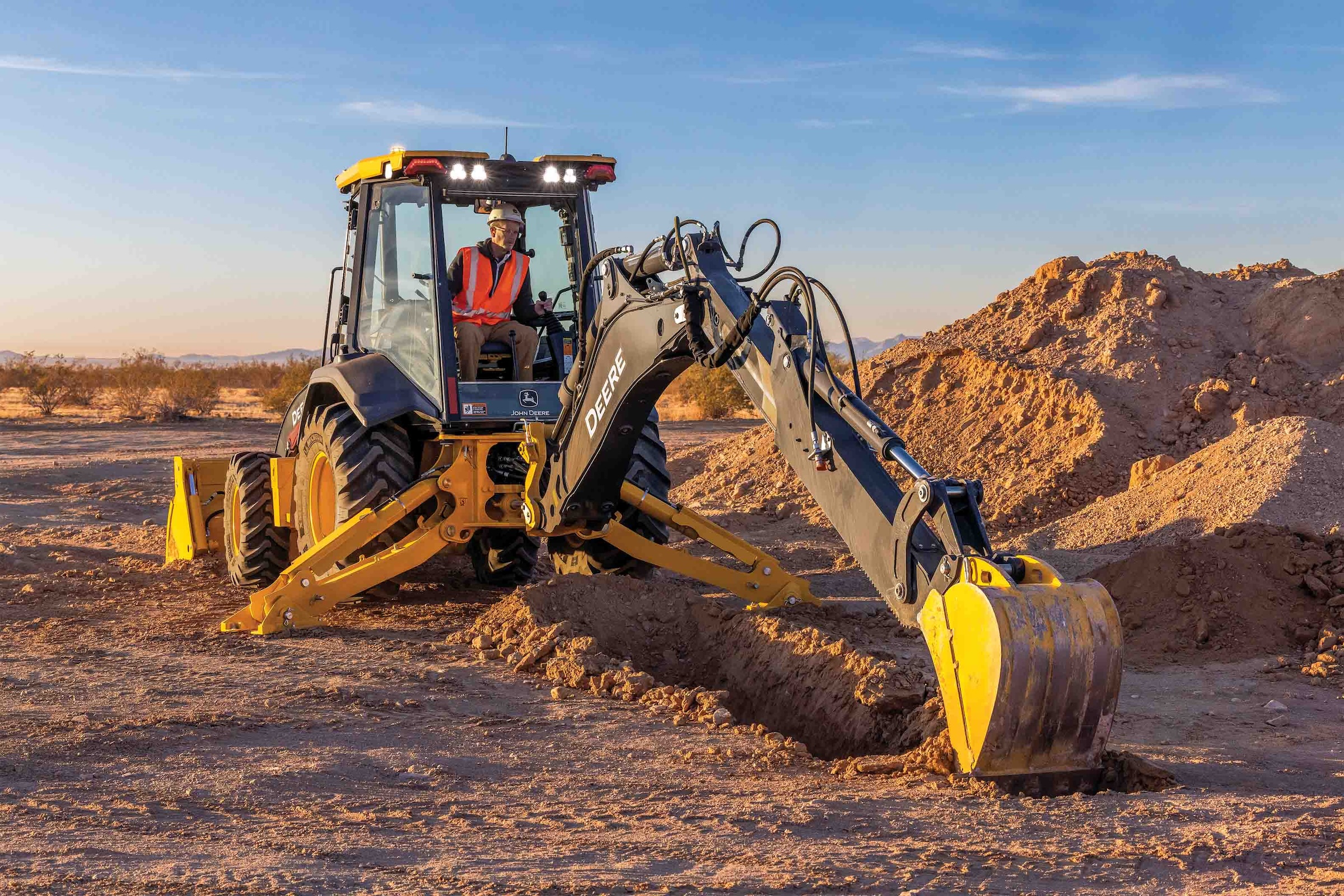 Yellow backhoe digging in desert terrain with yellow safety cones