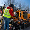 Construction workers operating a yellow asphalt paver on a road project