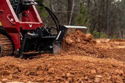 Yanmar construction machine moving red soil in wooded terrain