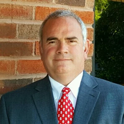 Professional man in blue suit and red polka dot tie standing by brick wall