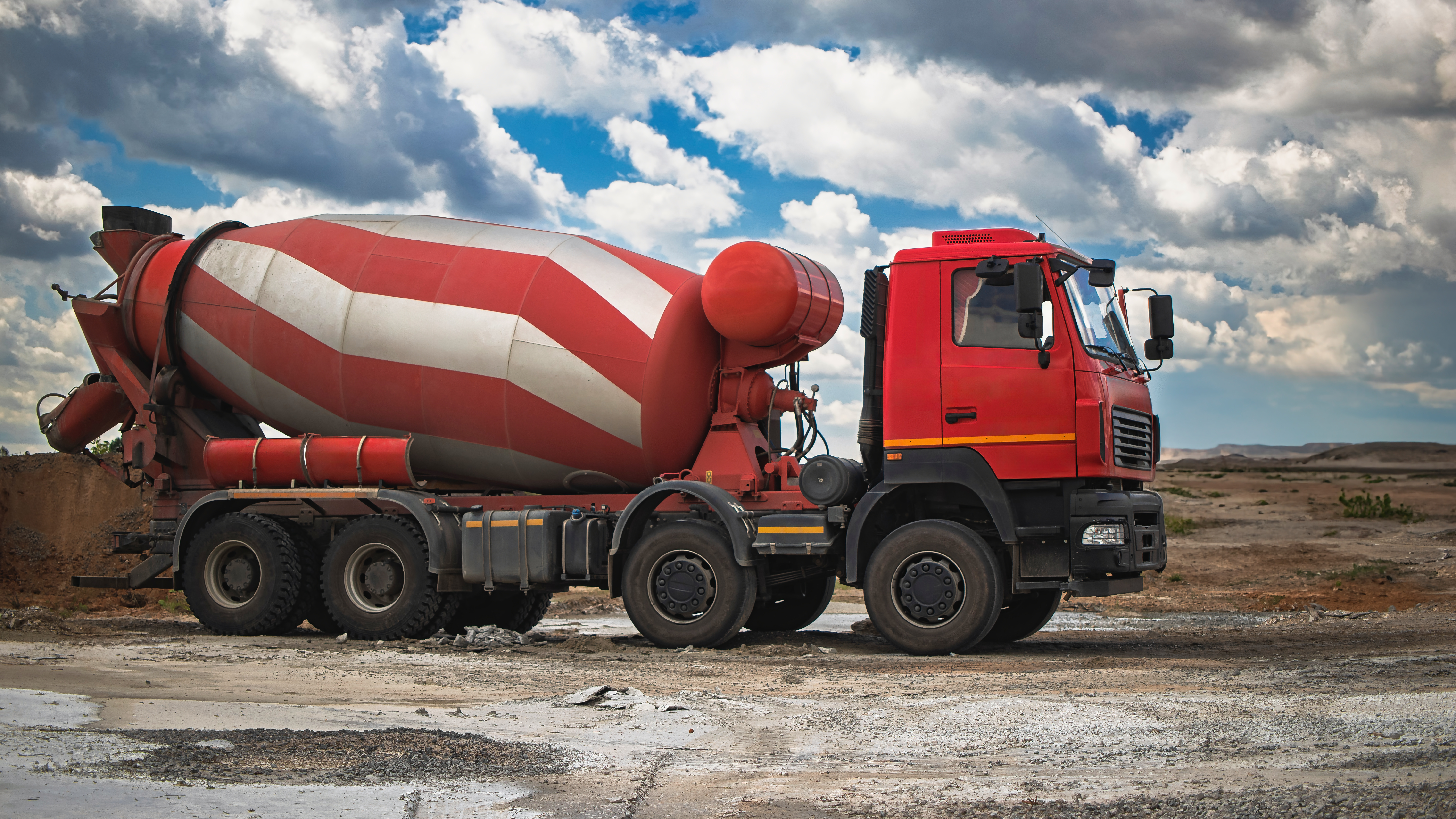 Red and white concrete mixer truck parked on rocky terrain under cloudy sky