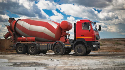 Red and white concrete mixer truck parked on rocky terrain under cloudy sky