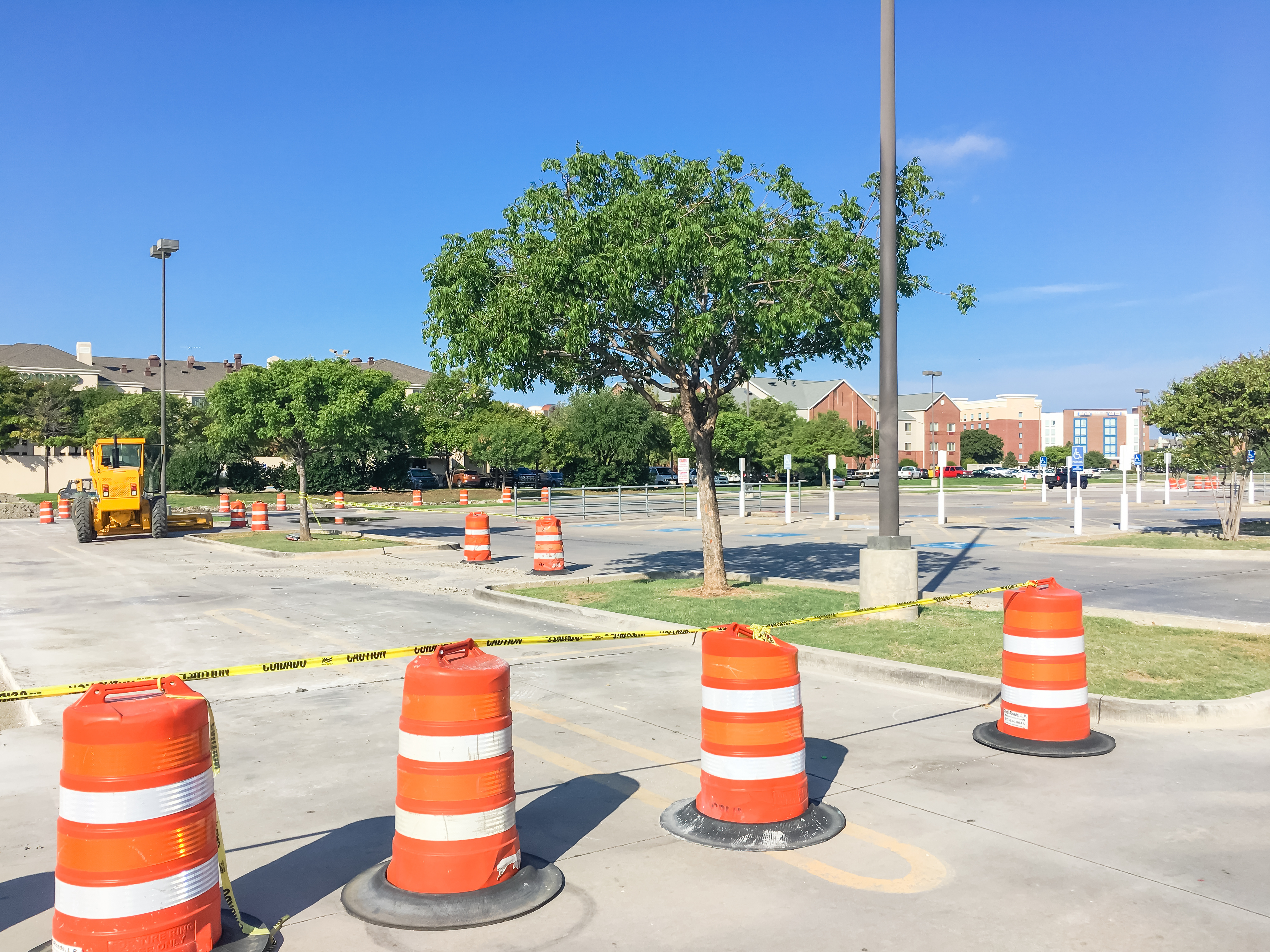 Construction site with orange traffic barrels and caution tape in parking lot