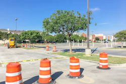 Construction site with orange traffic barrels and caution tape in parking lot