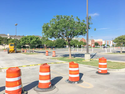Construction site with orange traffic barrels and caution tape in parking lot