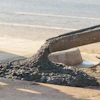 Wet concrete flowing from a construction chute onto a construction site surface