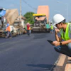 Construction worker in safety vest reviewing plans on roadside during asphalt paving project