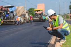 Construction worker in safety vest reviewing plans on roadside during asphalt paving project