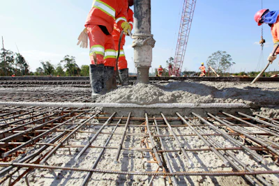 Construction workers pouring concrete over steel rebar grid at infrastructure project site