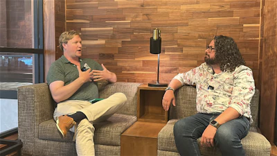 Two men sitting in chairs having a conversation in a wooden-paneled room