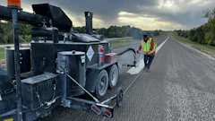 Road construction worker operating asphalt paving machine on highway at dawn