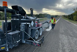 Road construction worker operating asphalt paving machine on highway at dawn
