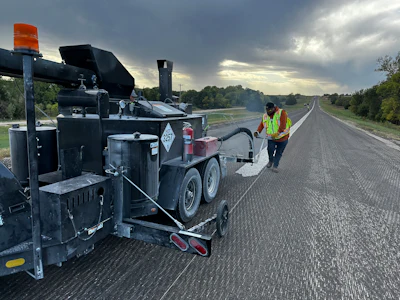 Road construction worker operating asphalt paving machine on highway at dawn