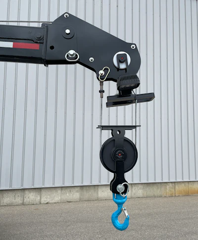 Black industrial crane mechanism with blue hook against metal wall