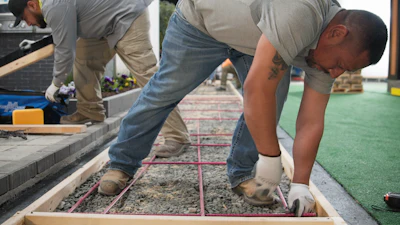 Construction workers installing pavers on outdoor ground with wooden frames