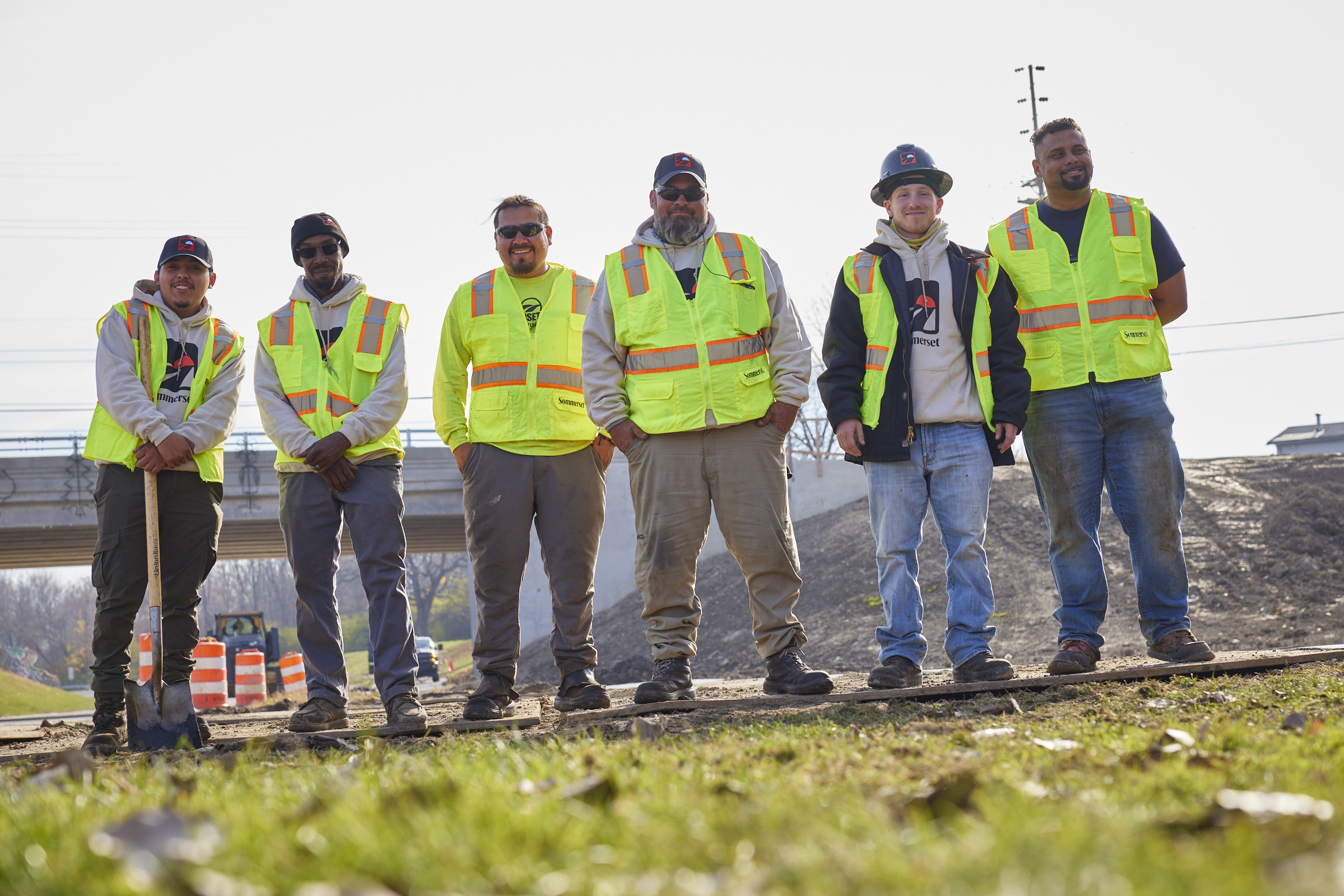 Six construction workers in bright safety vests standing on railroad tracks