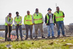 Six construction workers in bright safety vests standing on railroad tracks