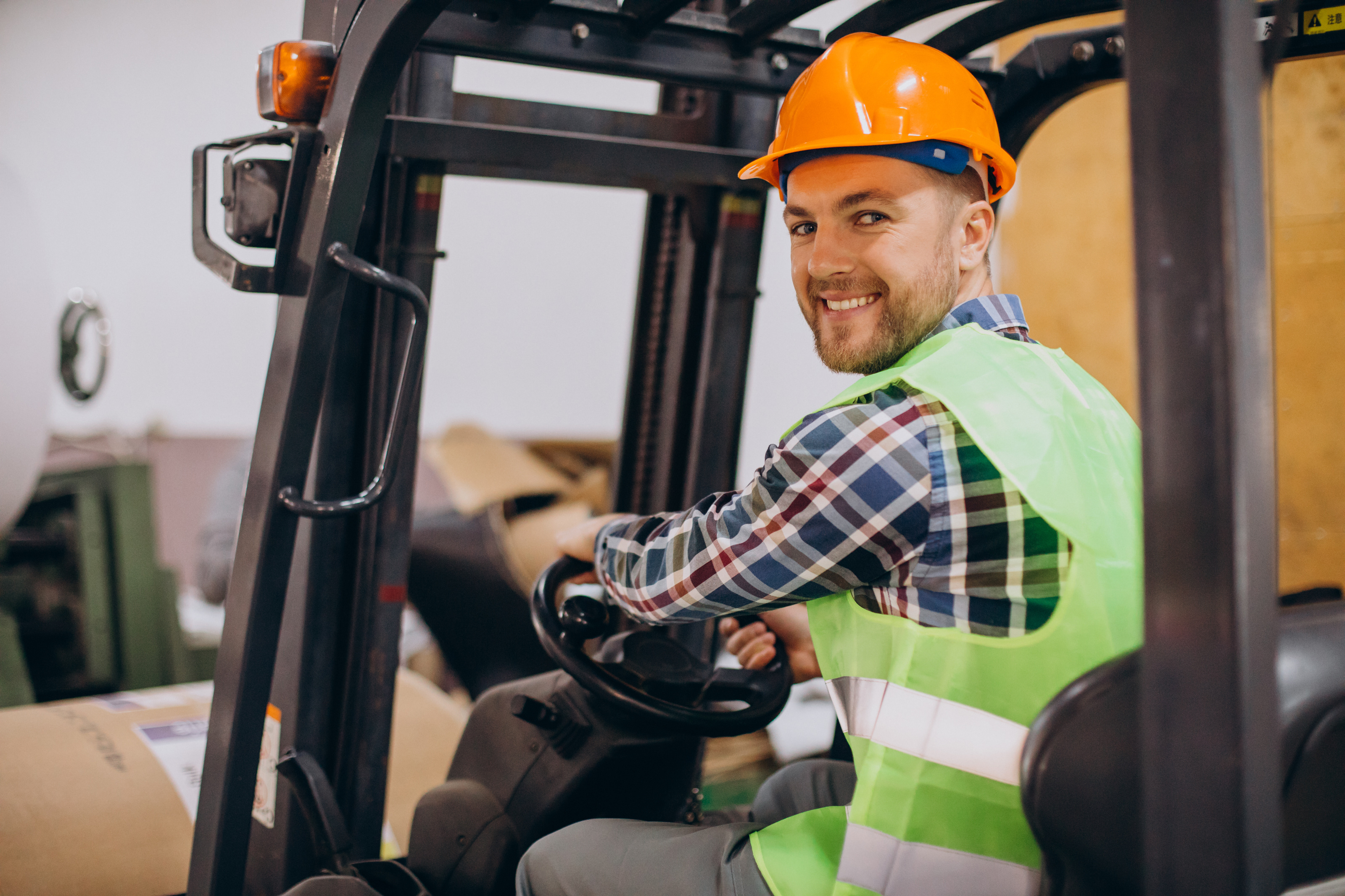 Smiling warehouse worker in safety gear operating a forklift