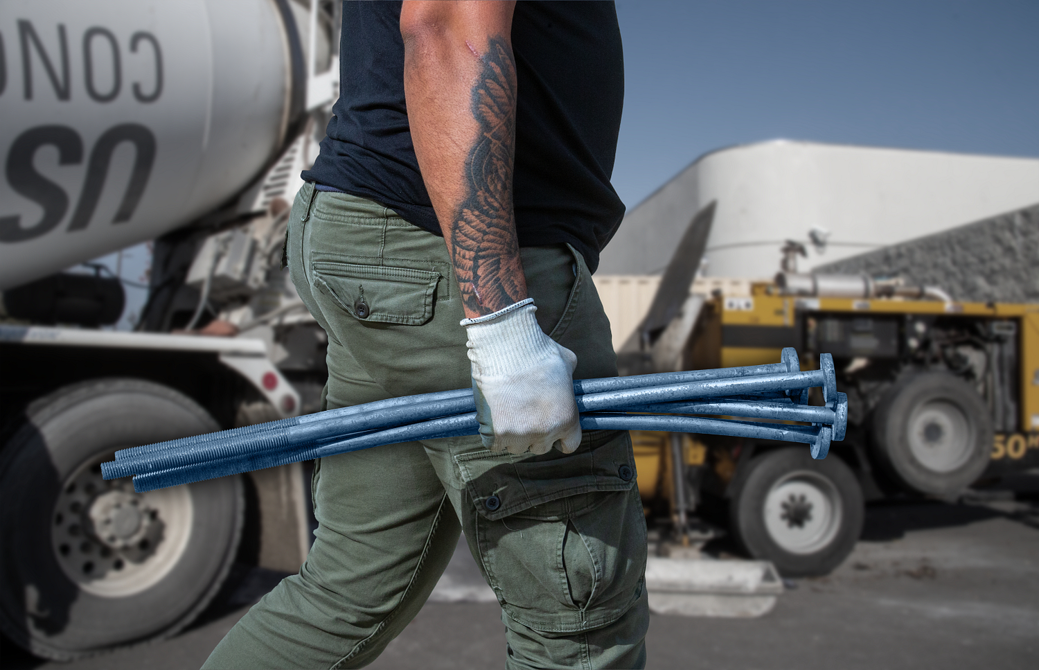 Construction worker carrying blue metal pipes near concrete mixer truck