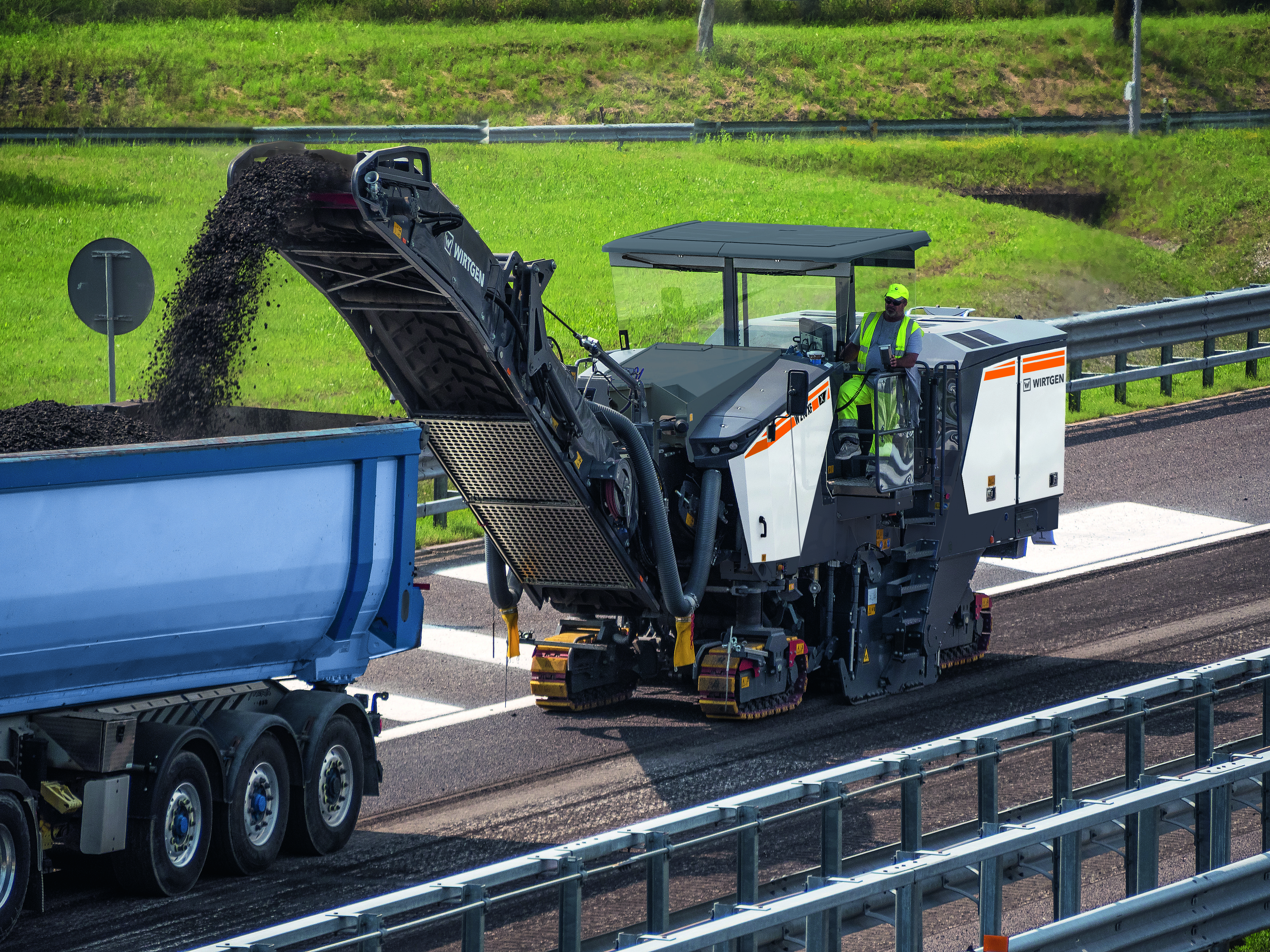 Road construction machine milling asphalt on highway with blue dump truck