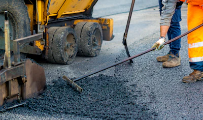 Road construction worker spreading fresh asphalt with paving machine