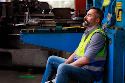 Tired worker in yellow safety vest resting near industrial machinery