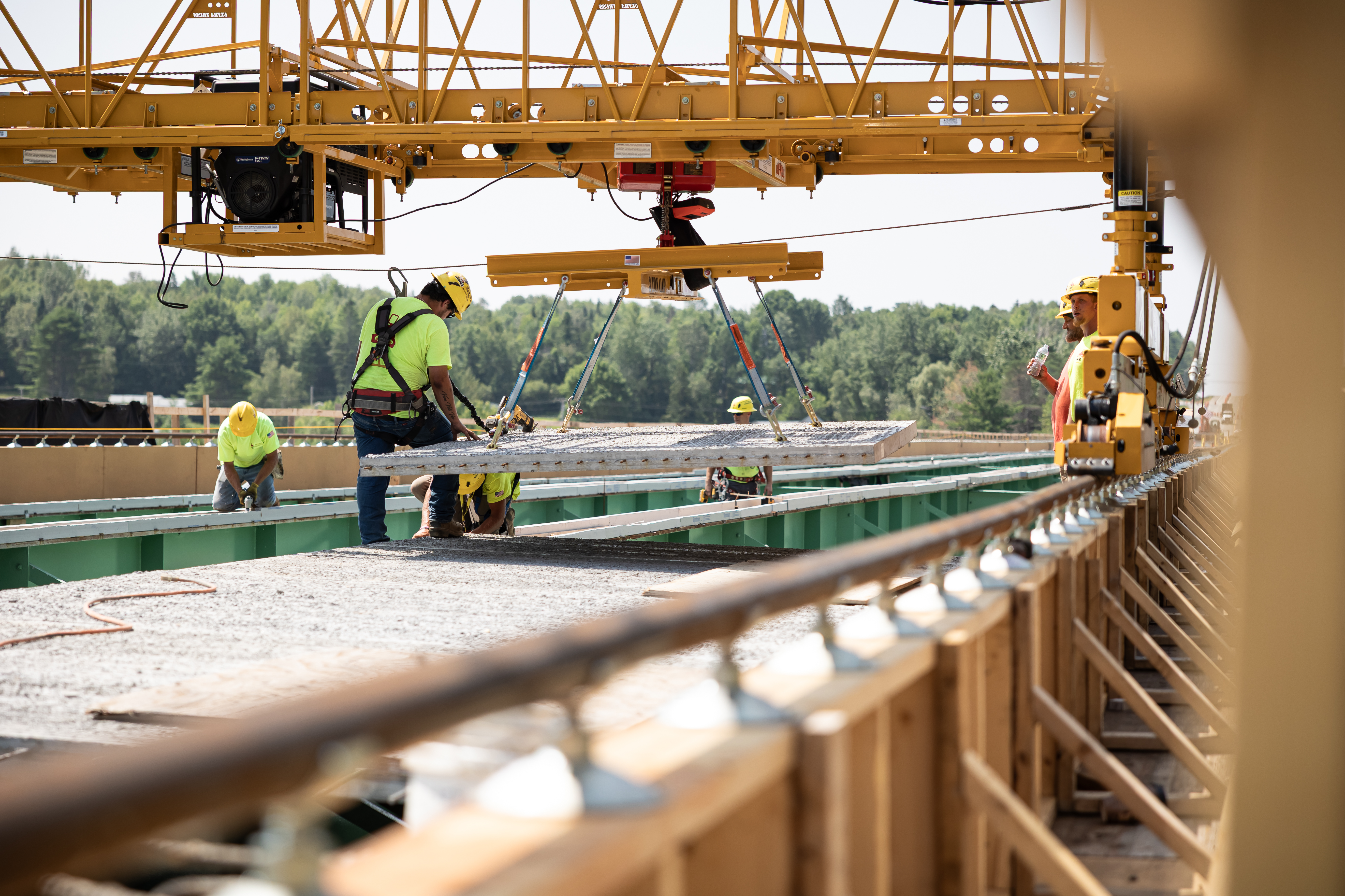 Construction workers installing concrete panels using overhead crane at infrastructure site