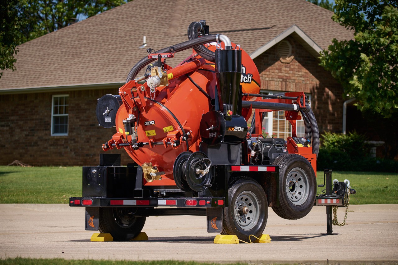 Red industrial vacuum truck trailer parked on concrete with brick house in background