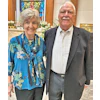 Smiling senior couple dressed formally, standing together in church setting with flowers