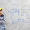 Young engineer in yellow hard hat studying architectural floor plan blueprint
