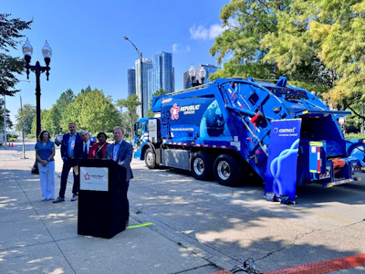 Blue Republic Services garbage truck at press conference with city skyline