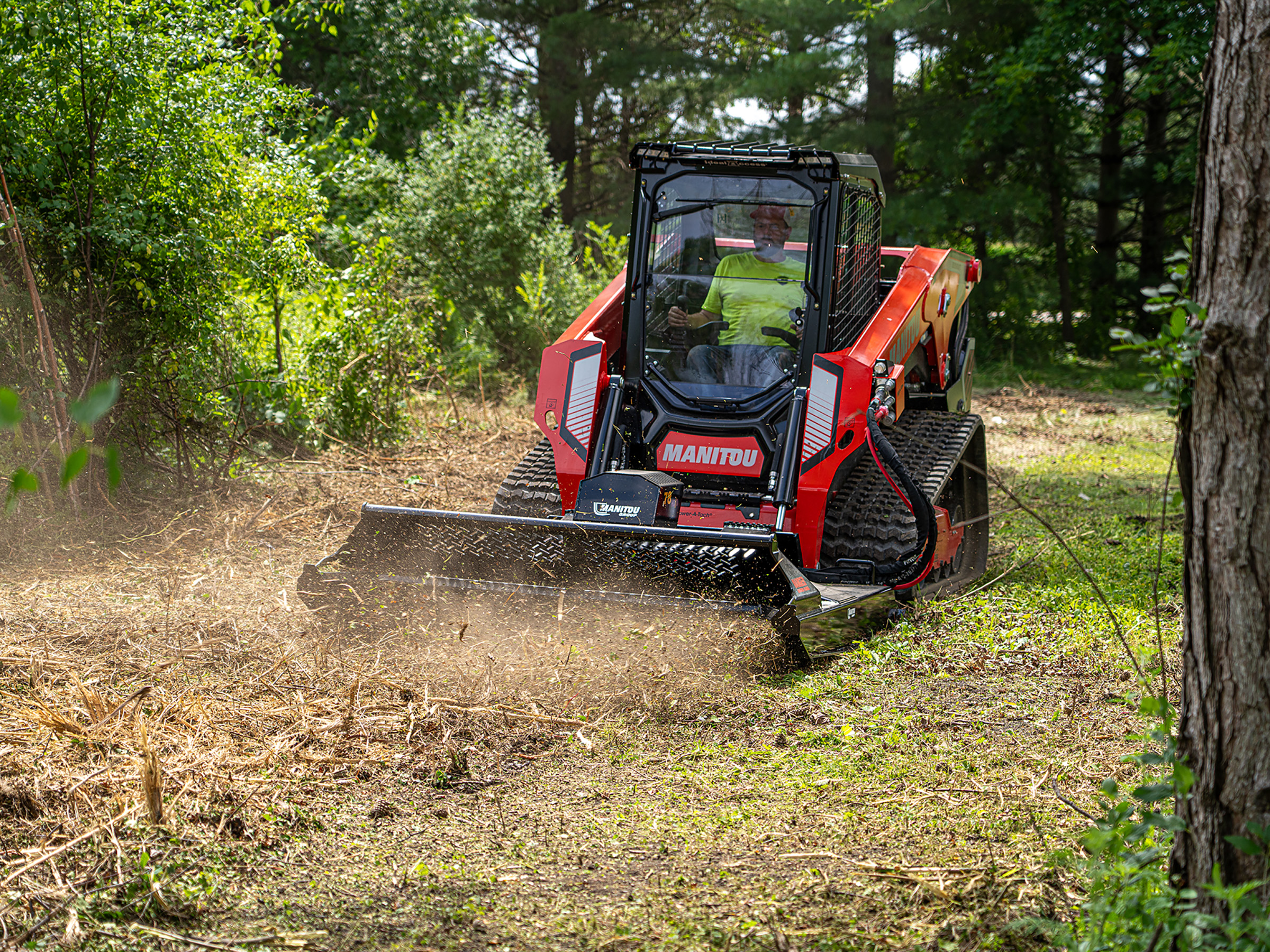 Red Manitou tracked skid steer mulching forest floor with brush attachment