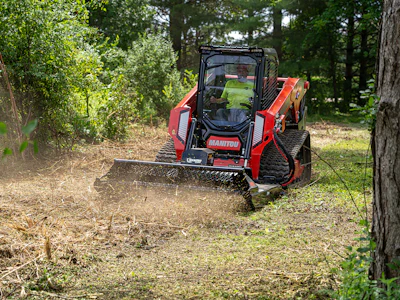 Red Manitou tracked skid steer mulching forest floor with brush attachment