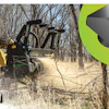 Yellow construction machine clearing brush in wooded area with dust flying
