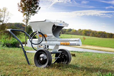 Silver Mud Mixer concrete equipment on wheels in grassy field with trees