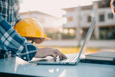 Construction worker using laptop at worksite with yellow hard hat